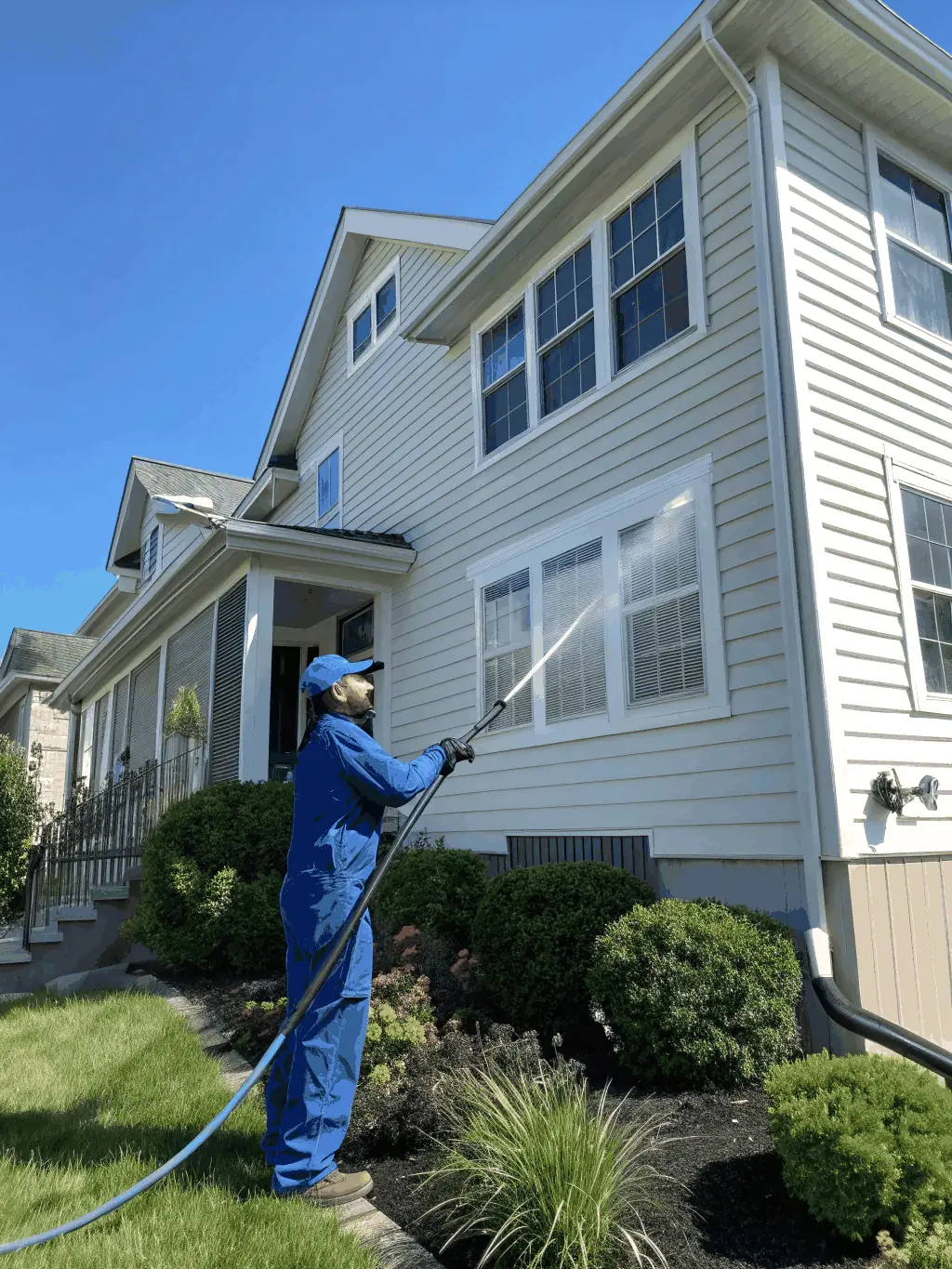 A technician power washing the siding of a brick and vinyl house, with gentle spray and visible dirt removal, surrounded by green landscaping typical of Louisville neighborhoods.